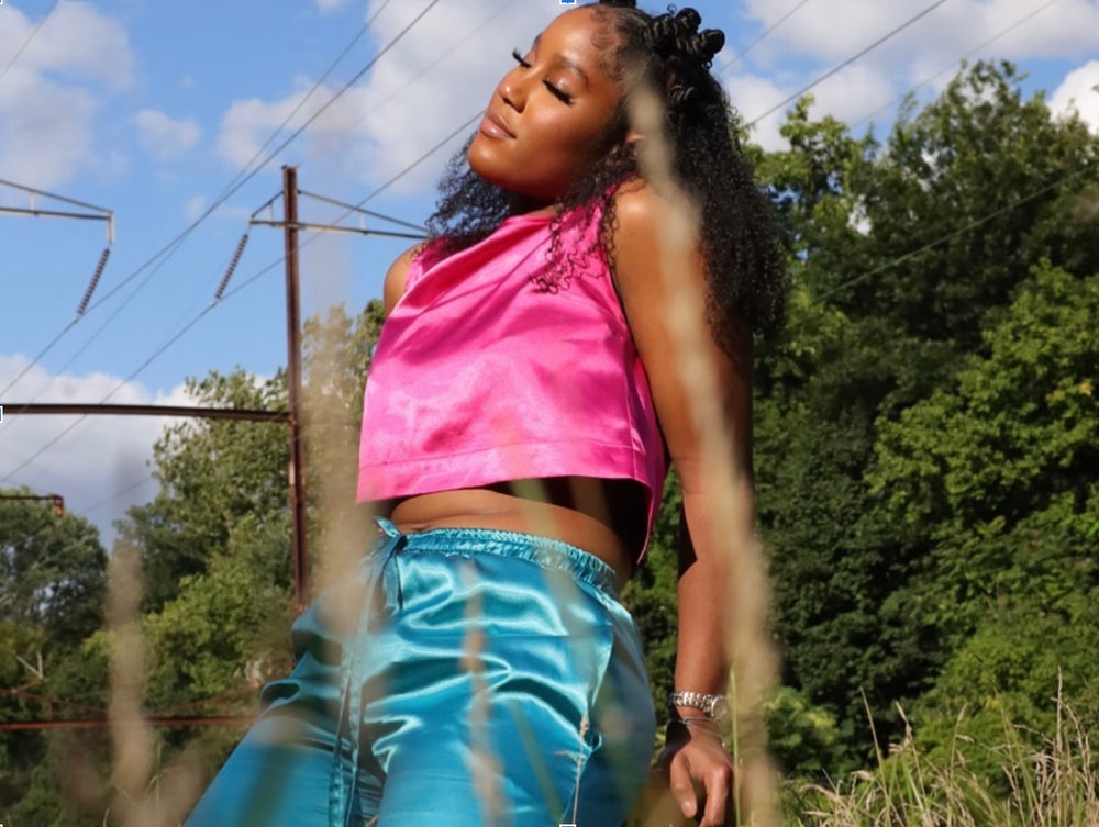 Woman in a pink satin top and blue satin pants sits in a field 